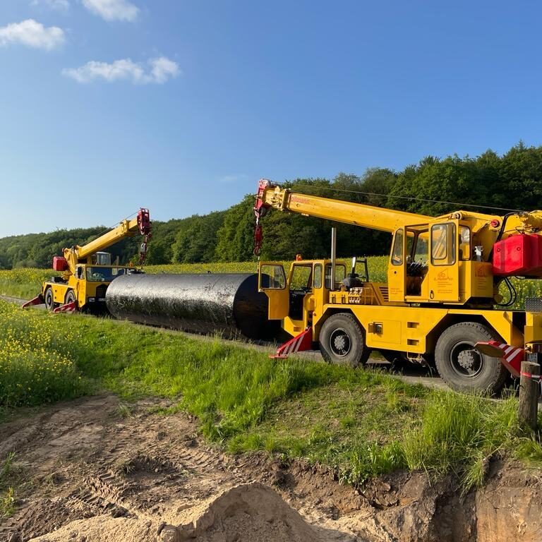 Zu sehen ist ein Löschwassertank der zwischen zwei Kränen eingespannt ist und im Tandemhub in eine Baugrube eingesetzt wird.